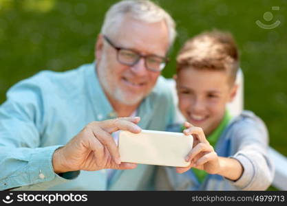 family, generation, technology and people concept - happy grandfather and grandson with smartphone taking selfie at summer park. old man and boy taking selfie by smartphone