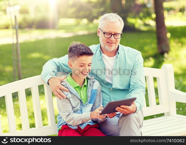 family, generation, technology and people concept - happy grandfather and grandson with tablet pc computer at summer park. grandfather and boy with tablet pc at summer park