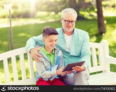 family, generation, technology and people concept - happy grandfather and grandson with tablet pc computer at summer park. grandfather and boy with tablet pc at summer park