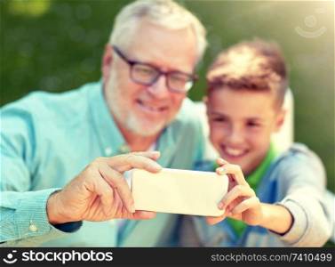 family, generation, technology and people concept - happy grandfather and grandson with smartphone taking selfie at summer park. old man and boy taking selfie by smartphone