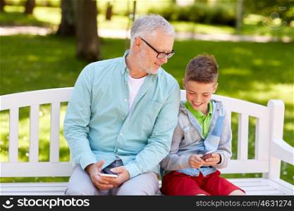 family, generation, technology and people concept - happy grandfather and grandson with smartphones at summer park