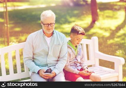 family, generation, technology and people concept - happy grandfather and grandson with smartphones at summer park. old man and boy with smartphones at summer park