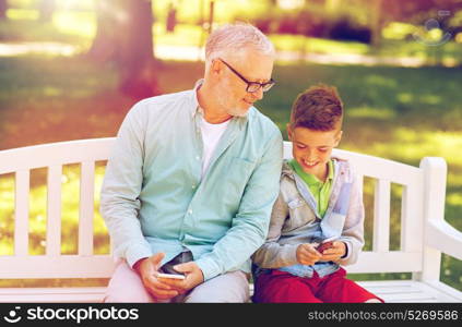 family, generation, technology and people concept - happy grandfather and grandson with smartphones at summer park. old man and boy with smartphones at summer park