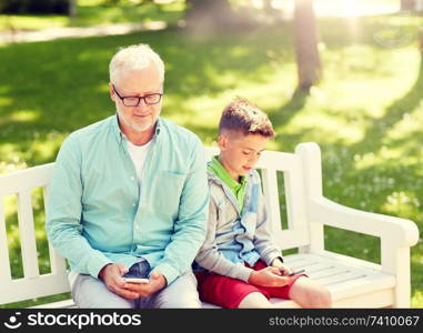 family, generation, technology and people concept - happy grandfather and grandson with smartphones at summer park. old man and boy with smartphones at summer park