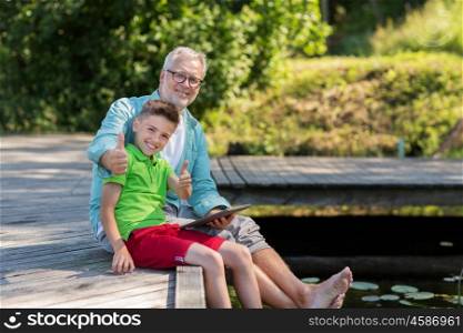 family, generation, technology, communication and people concept - grandfather and grandson with tablet pc computer sitting on river berth