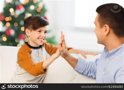 family, gesture and people concept - happy father and son doing high five at home over christmas tree background. happy father and son doing high five at christmas