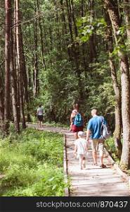 Family going a path in forest. Mother, father, boy and girl spending time together, vacations close to nature