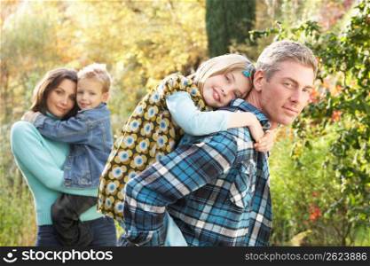 Family Group Outdoors In Autumn Landscape With Parents Giving Chiildren Piggyback