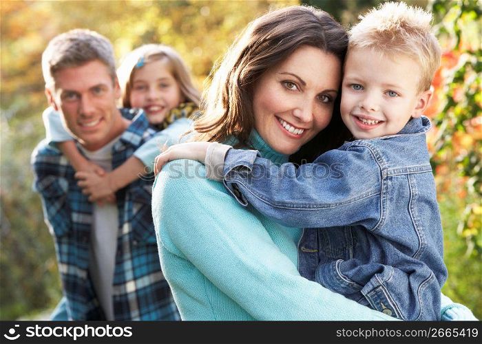 Family Group Outdoors In Autumn Landscape With Parents Giving Chiildren Piggyback