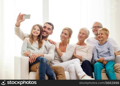 family, happiness, generation and people concept - happy family sitting on couch and making selfie with smartphone at home