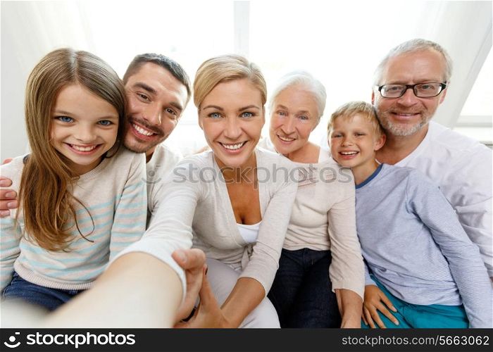 family, happiness, generation and people concept - happy family sitting on couch and making self portrait with camera or smartphone at home