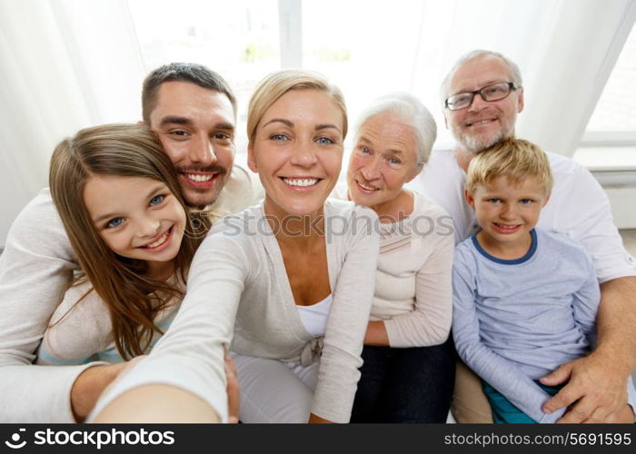 family, happiness, generation and people concept - happy family sitting on couch and making self portrait with camera or smartphone at home