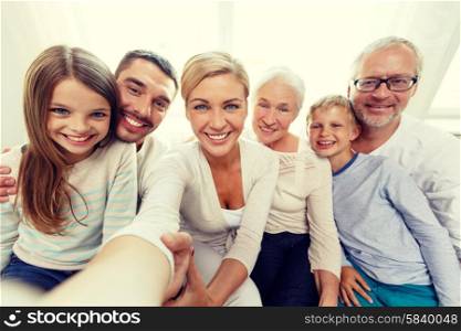 family, happiness, generation and people concept - happy family sitting on couch and making self portrait with camera or smartphone at home