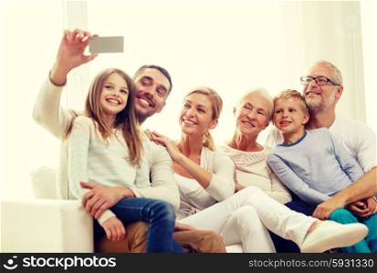 family, happiness, generation and people concept - happy family sitting on couch and making selfie with smartphone at home