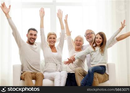 family, happiness, generation and people concept - happy family sitting on sofa and rising hands at home