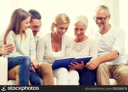 family, happiness, generation and people concept - happy family with book or photo album sitting on couch at home