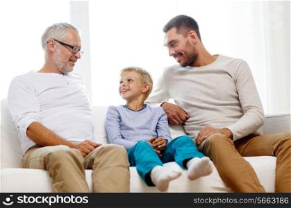 family, happiness, generation and people concept - smiling father, son and grandfather sitting on couch at home