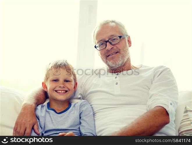family, happiness, generation and people concept - smiling grandfather with grandson sitting on couch at home