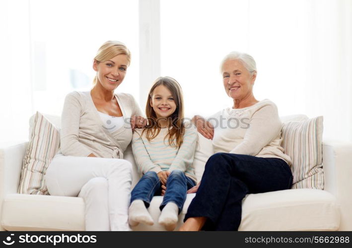 family, happiness, generation and people concept - smiling mother, daughter and grandmother sitting on couch at home