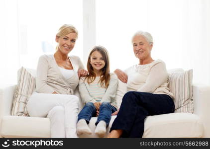 family, happiness, generation and people concept - smiling mother, daughter and grandmother sitting on couch at home