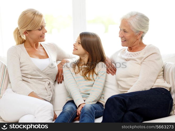 family, happiness, generation and people concept - smiling mother, daughter and grandmother sitting on couch at home