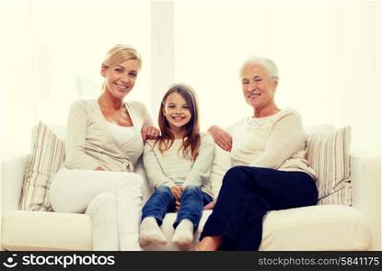 family, happiness, generation and people concept - smiling mother, daughter and grandmother sitting on couch at home