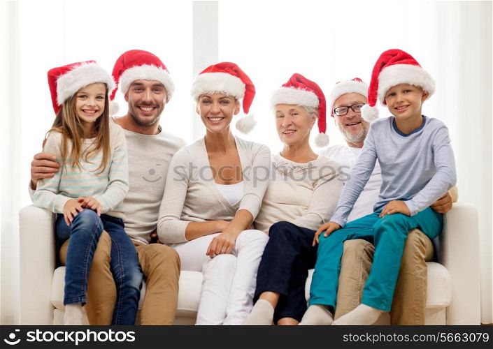 family, happiness, generation, holidays and people concept - happy family in santa helper hats sitting on couch at home