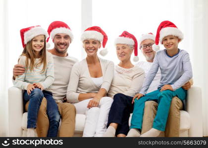 family, happiness, generation, holidays and people concept - happy family in santa helper hats sitting on couch at home