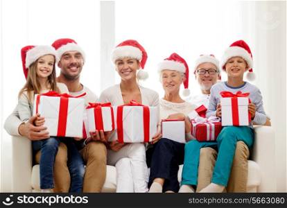 family, happiness, generation, holidays and people concept - happy family in santa helper hats with gift boxes sitting on couch at home