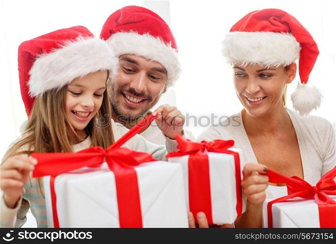 family, happiness, generation, holidays and people concept - happy family in santa helper hats with gift boxes sitting on couch at home