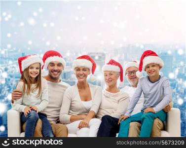 family, happiness, generation, holidays and people concept - happy family in santa helper hats sitting on couch over snowy city background