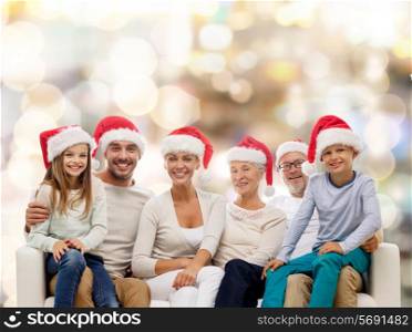 family, happiness, generation, holidays and people concept - happy family in santa helper hats sitting on couch over lights background