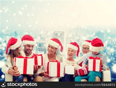 family, happiness, generation, holidays and people concept - happy family in santa helper hats with gift boxes sitting on couch over snowy city background