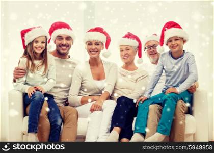 family, happiness, generation, holidays and people concept - happy family in santa helper hats sitting on couch at home