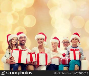 family, happiness, generation, holidays and people concept - happy family in santa helper hats with gift boxes sitting on couch over beige lights background