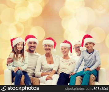 family, happiness, generation, holidays and people concept - happy family in santa helper hats sitting on couch over beige lights background