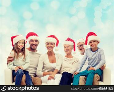 family, happiness, generation, holidays and people concept - happy family in santa helper hats sitting on couch over blue lights background