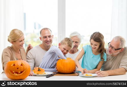 family, happiness, generation, holidays and people concept - happy family making halloween pumpkins at home