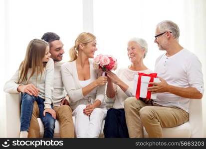 family, happiness, generation, holidays and people concept - happy family with bunch of flowers and gift box sitting on couch at home