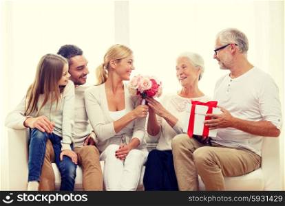 family, happiness, generation, holidays and people concept - happy family with bunch of flowers and gift box sitting on couch at home