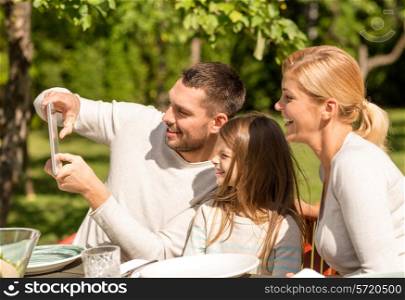family, happiness, generation, home and people concept - happy family sitting at table and taking selfie with tablet pc computer outdoors