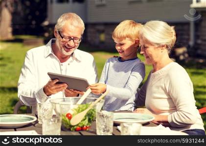 family, happiness, generation, home and people concept - happy family sitting at table with tablet pc computer outdoors