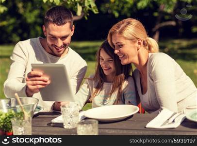 family, happiness, generation, home and people concept - happy family sitting at table with tablet pc computer outdoors