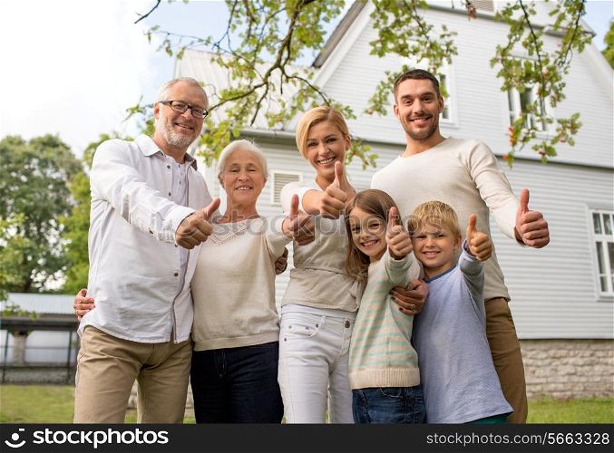 family, happiness, generation, home and people concept - happy family standing in front of house and showing thumbs up outdoors
