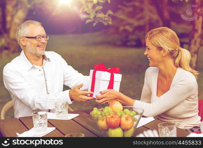 family, happiness, generation, home and people concept - happy family with gift box having holiday dinner outdoors