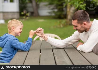 family, happiness, generation, home and people concept - happy father and son doing arm wrestling outdoors