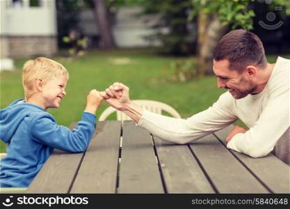 family, happiness, generation, home and people concept - happy father and son doing arm wrestling outdoors