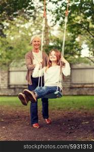 family, happiness, generation, home and people concept - happy grandmother and granddaughter swinging on teeterboard outdoors