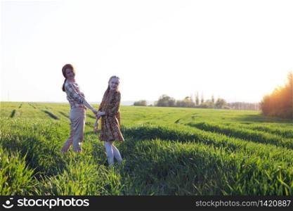 family - happy mother and daughter on a field on the sunset