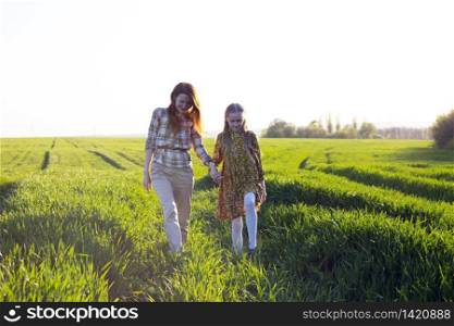 family - happy mother and daughter walk on the field at sunset
